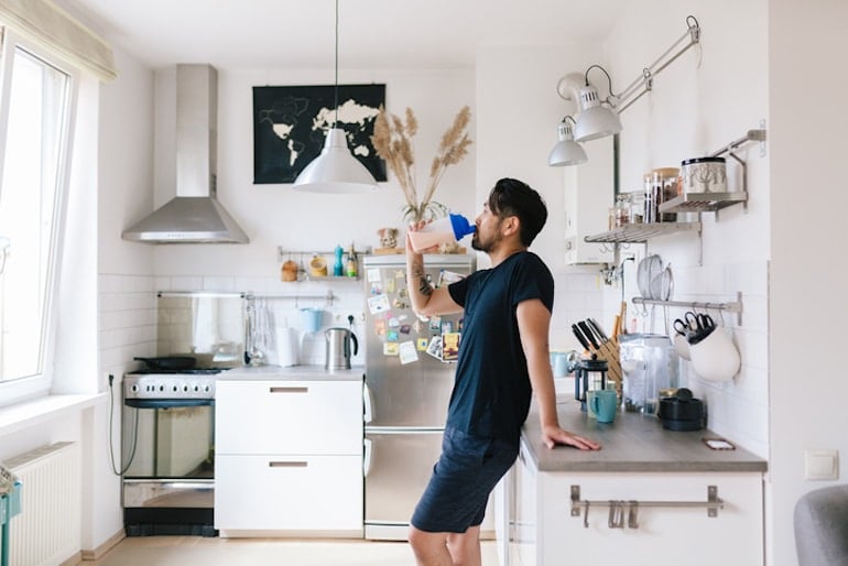 Man drinking a protein shake in his kitchen after a workout to balance blood sugar and avoid cravings