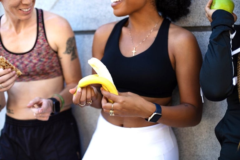 Group of women after a workout, with one of them peeling a banana since it's a great healthy food for energy