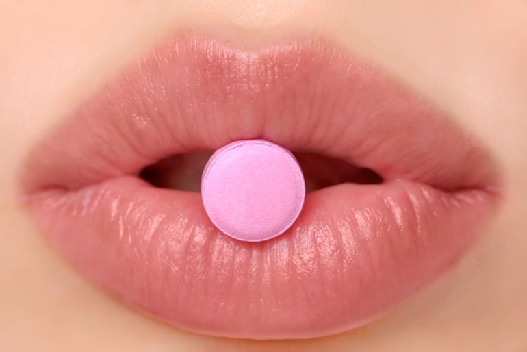 Woman with a pink birth control pill between her lips