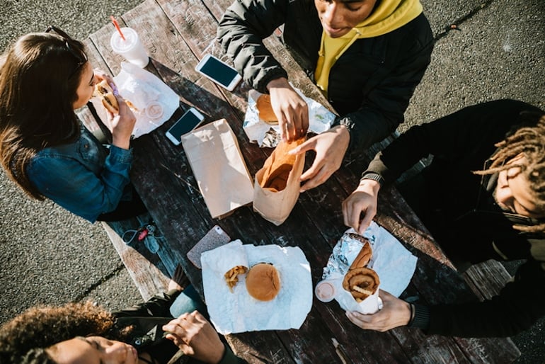 Group of friends eating fast food outdoors to indulge their carb cravings