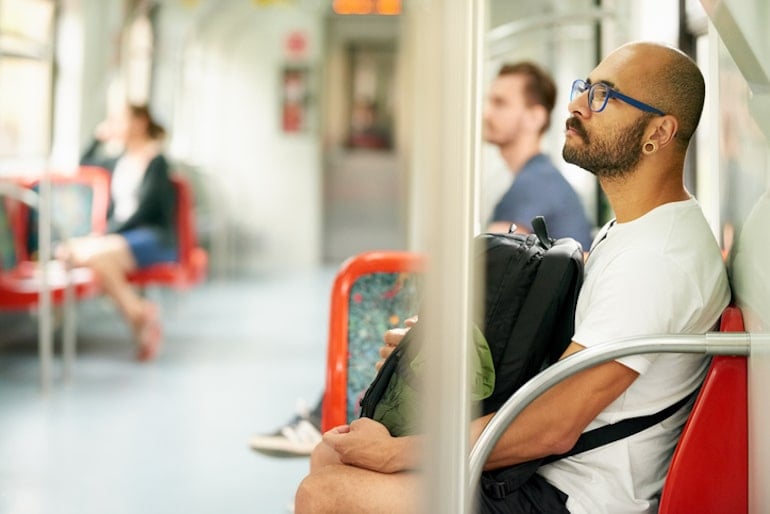 Balding man on public transportation wondering about the causes of male pattern baldness