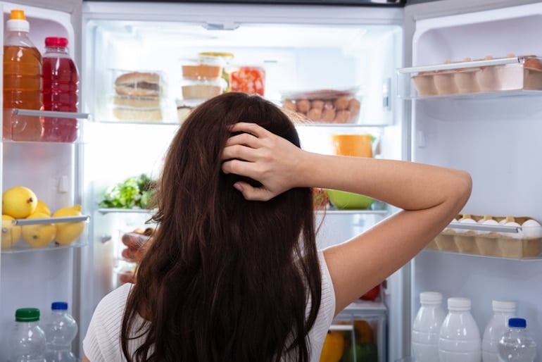 Shot from behind of brunette woman looking into fridge, wondering what to eat during her intermittent fasting open eating window