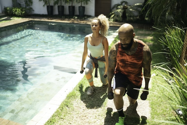 Man and woman doing functional fitness lunges with weights next to their pool