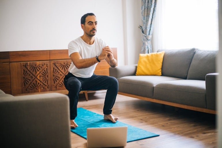 Man doing squats on a blue yoga mat in his living room