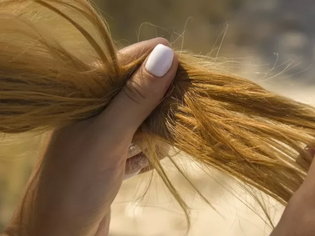 Red-headed woman looking at her hair and wondering how to make your hair less greasy