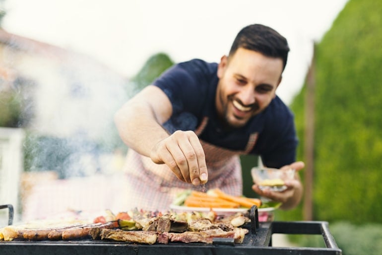 Man seasoning meat and veggies on a grill