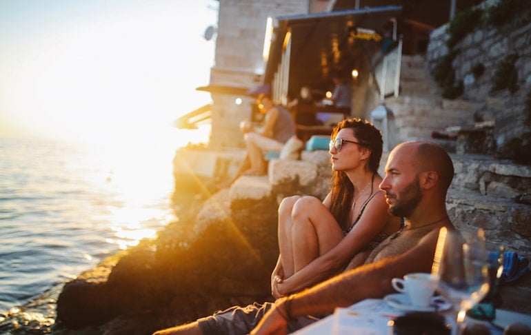 Bald man with a woman on a cliff by the sea looking out into the sunset