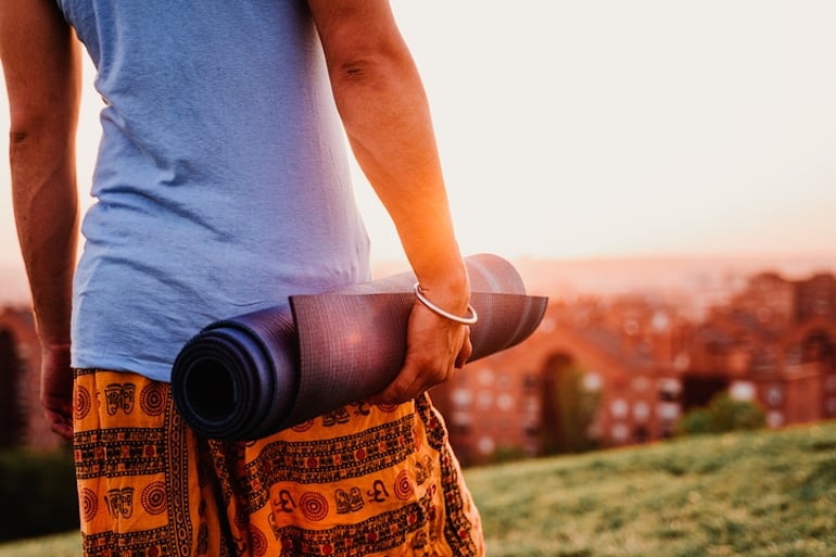 Young man holding yoga mat in park, ready to practice yoga and meditate to manage stress and thus prevent hair loss from stress