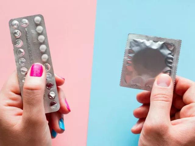 Woman's hand holding pack of birth control pills on pink background and man's hand holding a condom on blue background