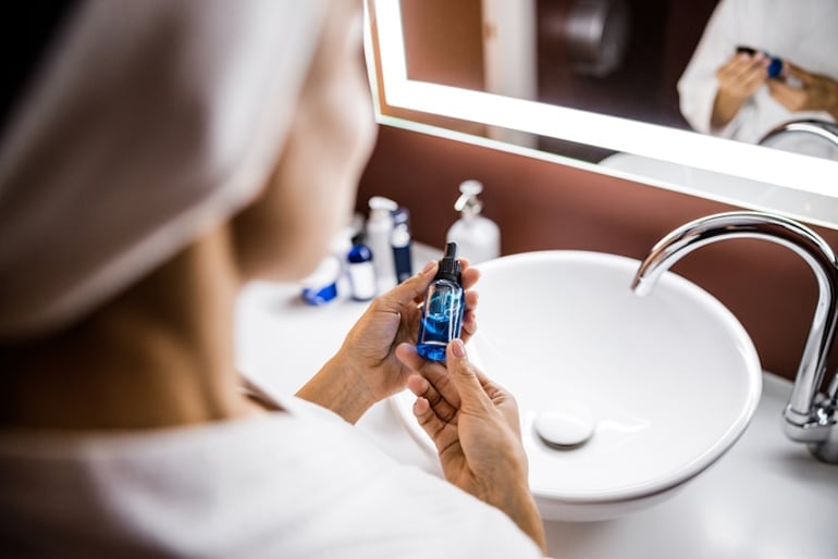 Woman holding a serum at her bathroom vanity