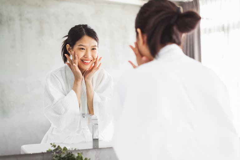 Woman looking in the mirror at her beautiful, clear skin thanks to using the best serum for her skin type and concerns