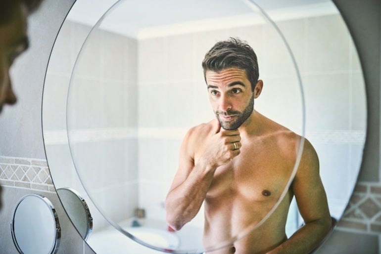 Man looking in bathroom mirror at his great skin thanks to the powerful benefits of face serum