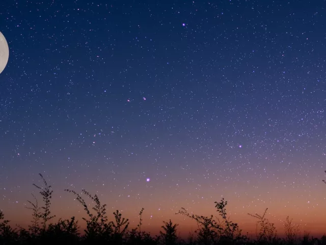Full moon over a field amidst a purple and orange starry night sky