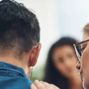 Woman consoling crying husband in a therapy setting, getting his emotions out to reap the benefits of crying