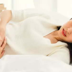 Woman laying in bed suffering from cramps as a common PMS symptom