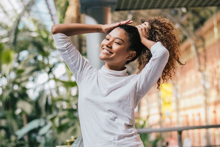 Woman putting up her curly hair, treated with the best hair oils, outdoors