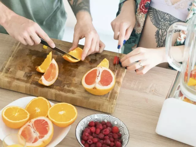 Couple making a morning smoothie at the kitchen island with foods that pack the best vitamins for glowing skin, such as vitamin C