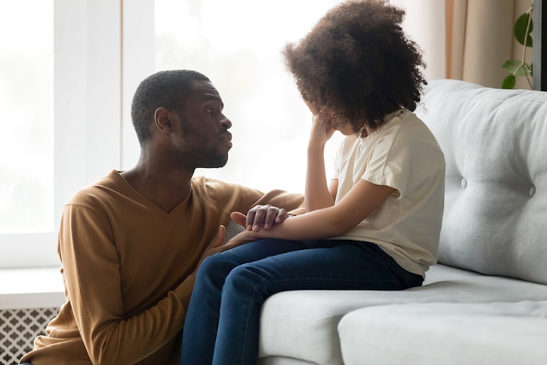 Father soothing crying daughter on the couch