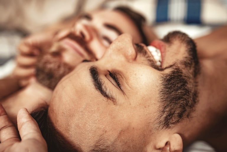 Gay couple in bed after sex, smiling with the post-coital glow