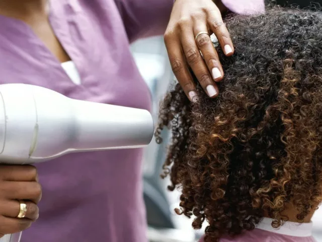 Side profile of a Black woman drying her natural hair at a salon