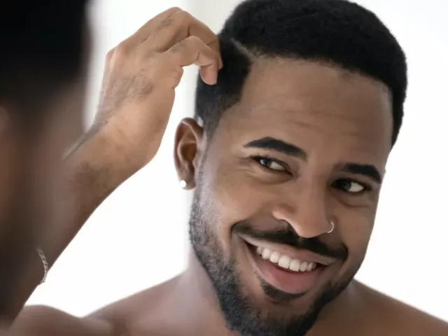 Black man running fingers through his hair, wondering if he should use coconut oil