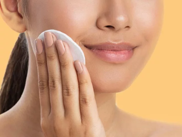 Woman exfoliating her sensitive skin with lactic acid toner on a cotton pad