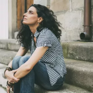 Woman sitting on steps curled up from stress due to hormone imbalances, looking at the sky