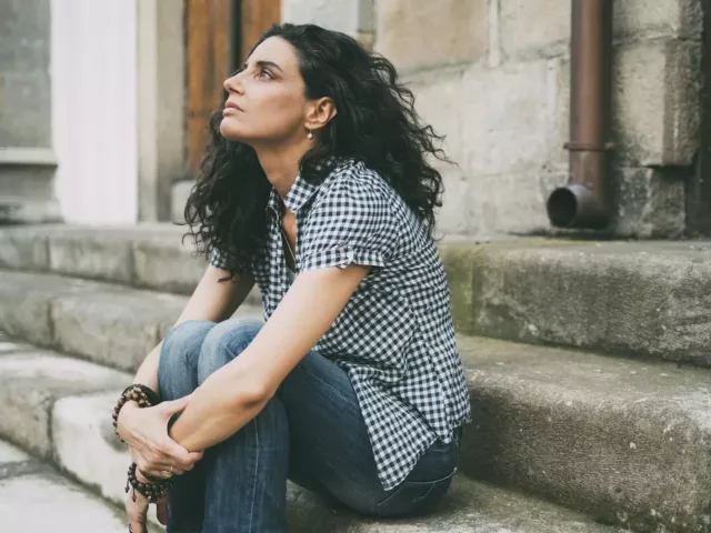 Woman sitting on steps curled up from stress due to hormone imbalances, looking at the sky