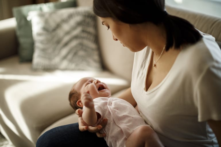 New mother holding a crying baby, stressed out from postpartum hormonal imbalances