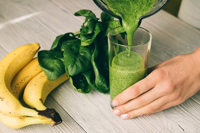 Woman pouring a smoothie with spinach from blender to boost her hyaluronic acid levels