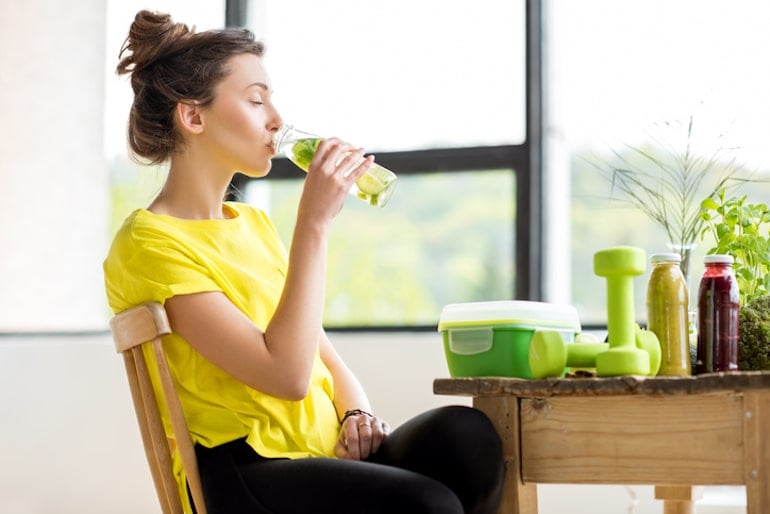 Woman drinking water infused with fruit and taking the best vitamins for glowing skin