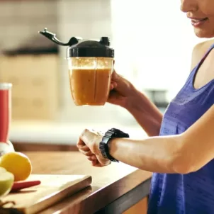 Active woman drinking a smoothie and looking at her watch to determine the best time to take probiotics