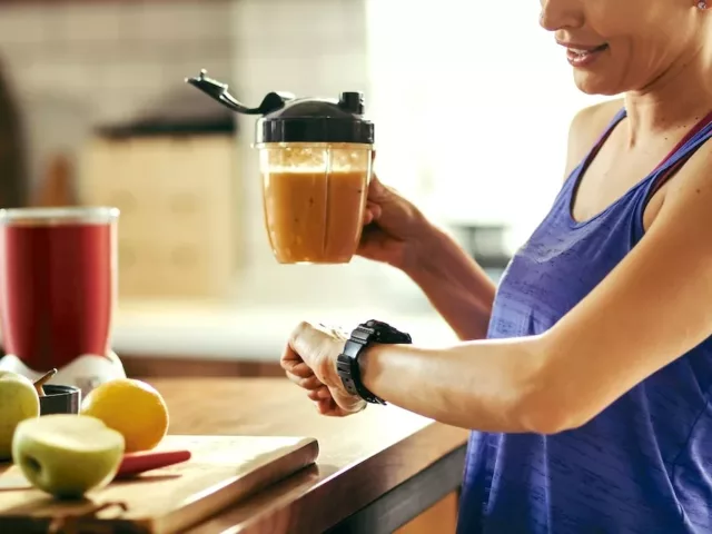 Active woman drinking a smoothie and looking at her watch to determine the best time to take probiotics