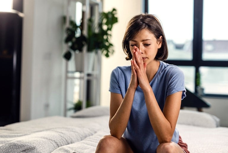 Anxious woman sitting on bed with her mouth resting on her hands, trying to balance her hormones for their mental health repurcussions