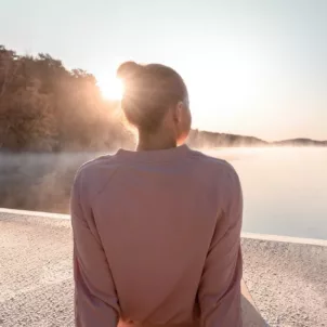 Woman sitting by a lake at sunrise, enjoying the minimal lifestyle, simple joy of living, and psychological benefits of minimalism