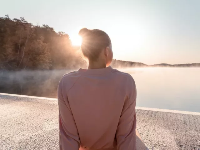 Woman sitting by a lake at sunrise, enjoying the minimal lifestyle, simple joy of living, and psychological benefits of minimalism