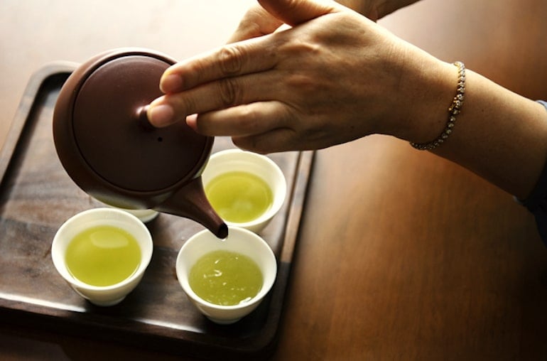 Woman pouring green tea in glasses, one of the best foods for brain health thanks to antioxidants and caffeine