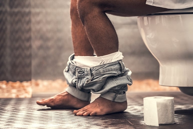 Man on toilet to illustrate butt care, healthy bowel movements, and anal health