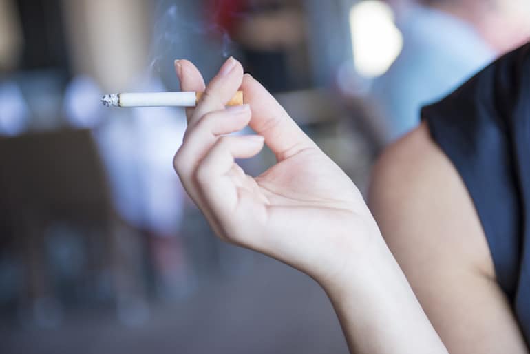 Female hand holding a cigarette; the smoke is a major source of free radicals and oxidative stress