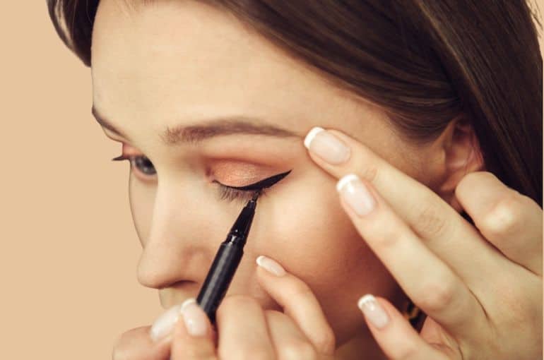 Woman tugging on eye to do her makeup, which can prematurely age skin and cause wrinkles to form