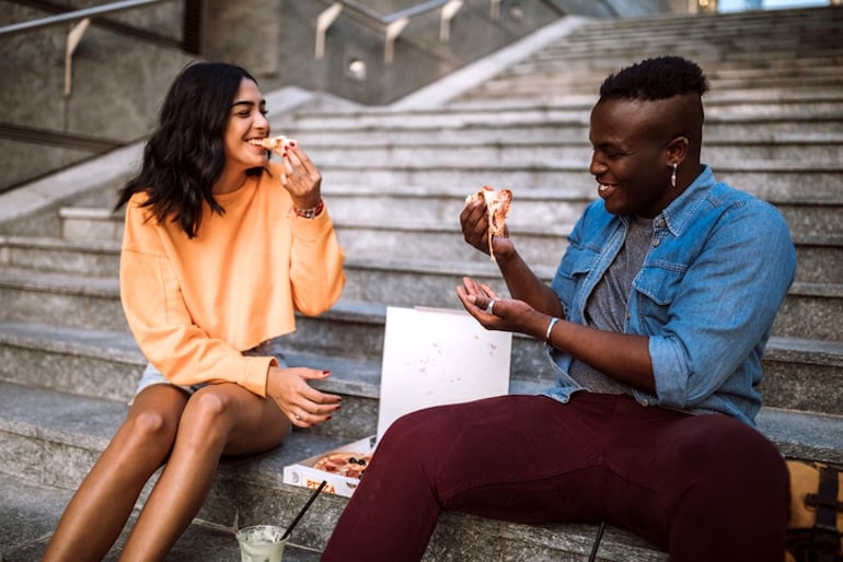 Young couple eating pizza outdoors, a food that can produce free radical damage