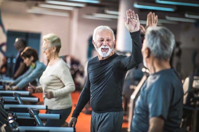 Happy senior men high-fiving at the gym, illustrating positivity and happiness as the best things that get better with age