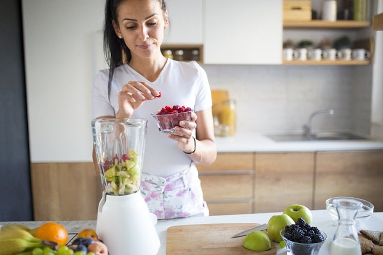 Woman making a smoothie with apples and raspberries, two antioxidant-rich foods that can help reduce free radicals in the body