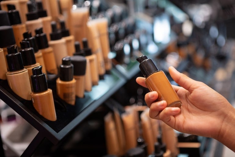 Woman choosing makeup at beauty counter, making sure to pass on makeup ingredients to avoid that could lead to premature skin aging