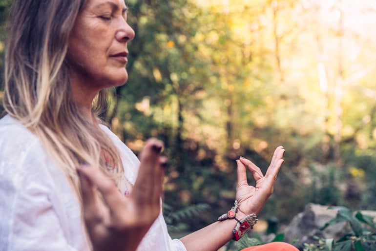 Menopausal woman meditating in a forest to help reduce the severity of hot flashes