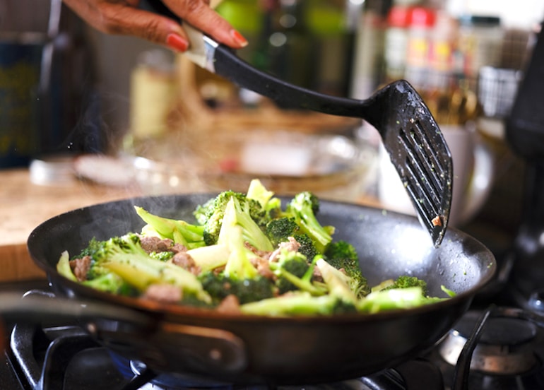 Menopausal woman cooking broccoli on the stove, rich in vitamin E