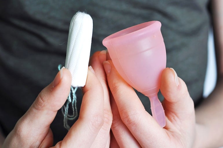 Woman holding an organic tampon and pink menstrual cup