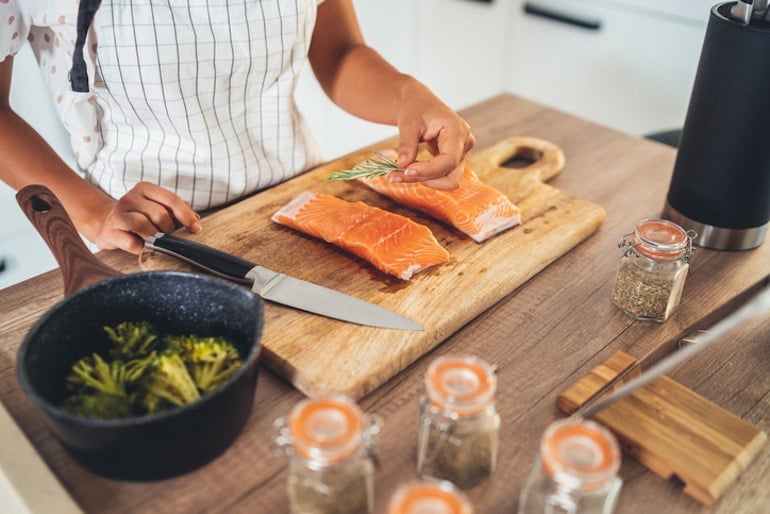 Woman preparing salmon with broccoli, two of the best foods for brain health and cognition