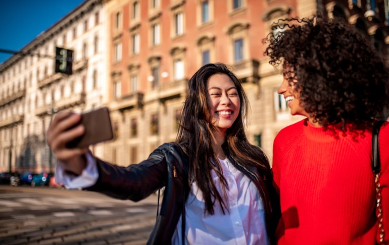 Two women outside posing for a selfie, though the flash and too much screen time can lead to wrinkles, hyperpigmentation, and other skin damage