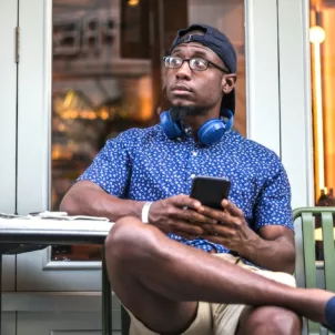 Concerned wearing a hat at cafe on phone, searching if hats cause hair loss in men